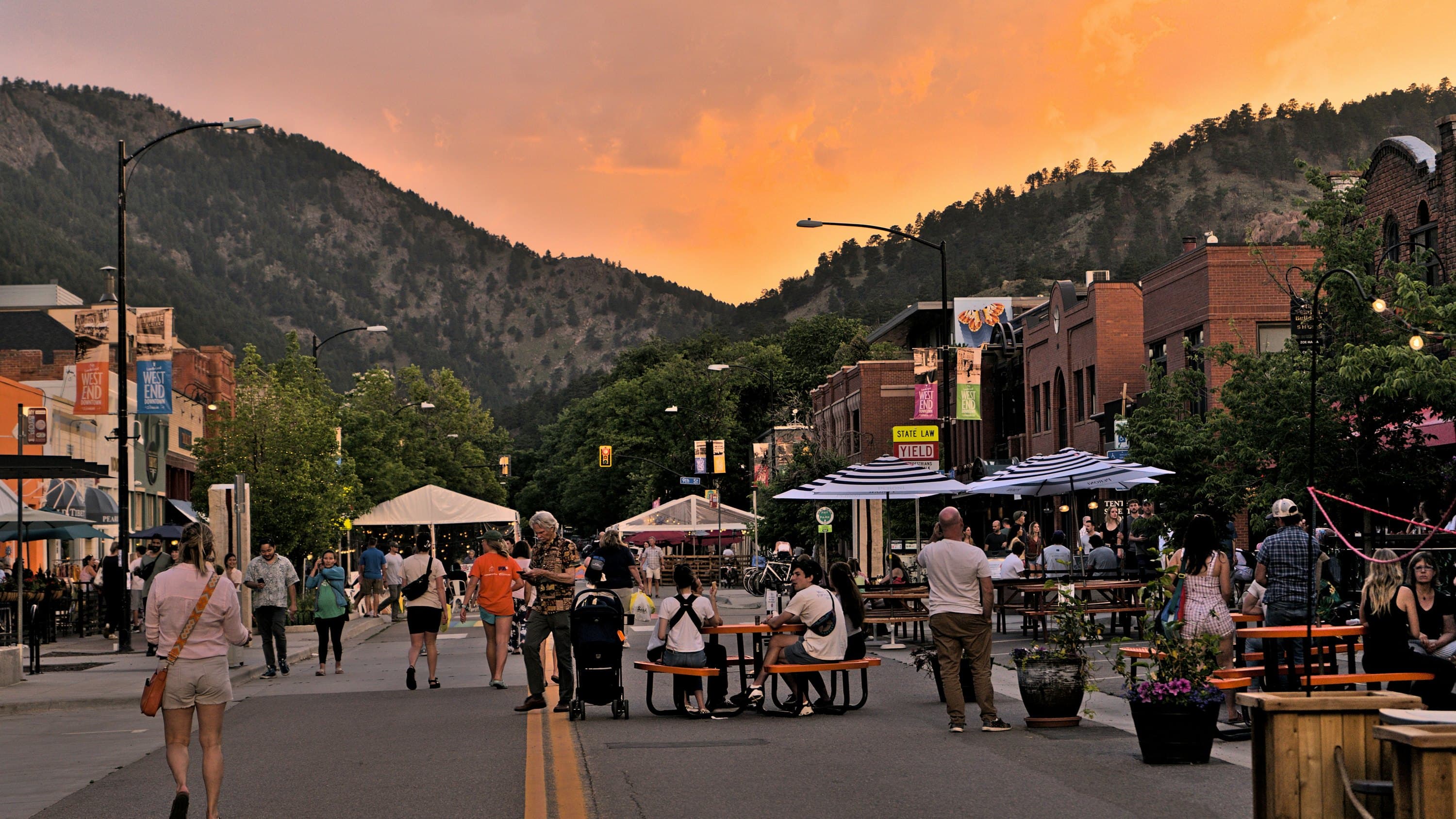 downtown boulder at sunset, people at picnic tables down a closed street, the foothills lit pink behind