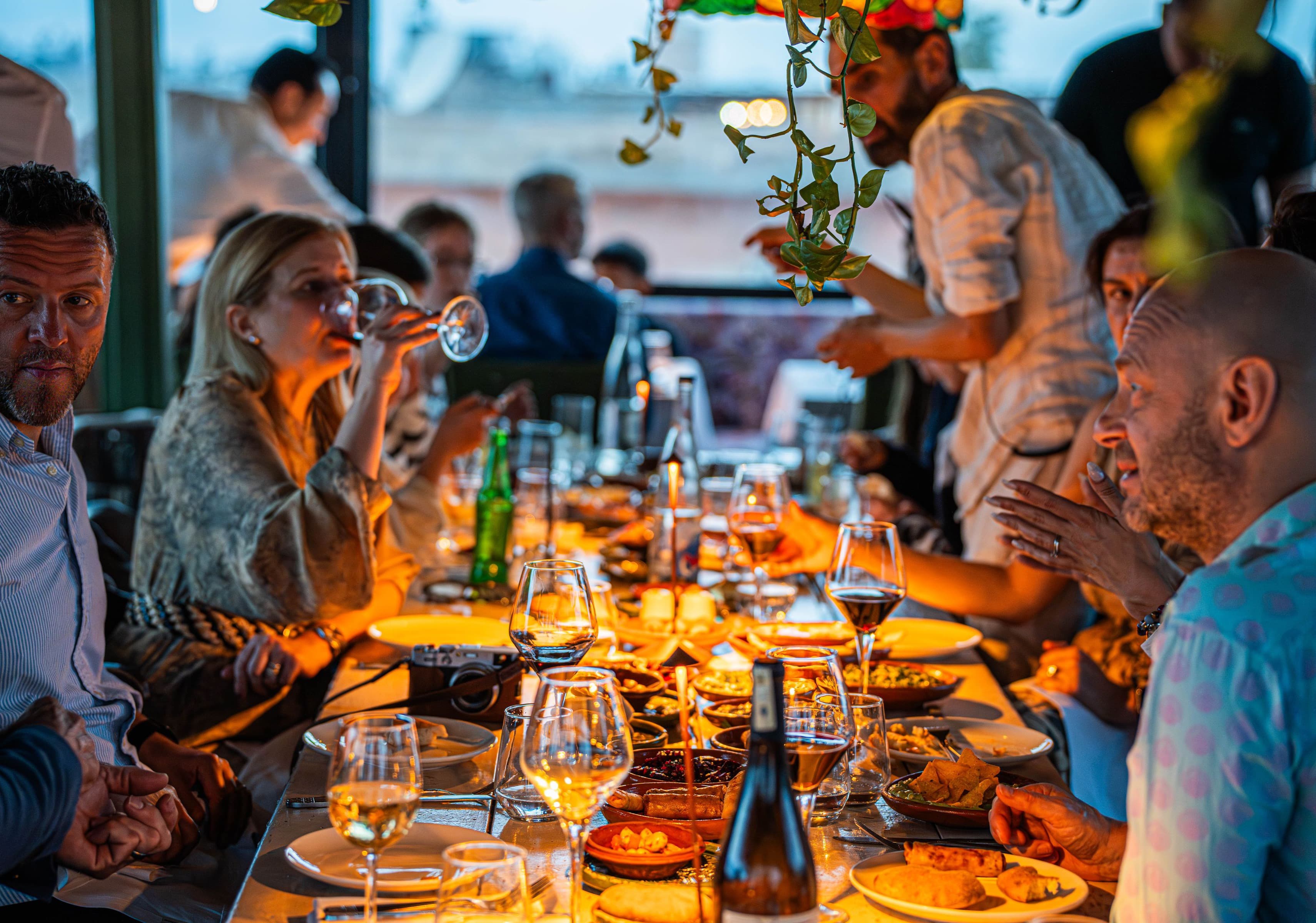a long table seen from its head, every seat taken, amber candle and lamp light, ivy overhead