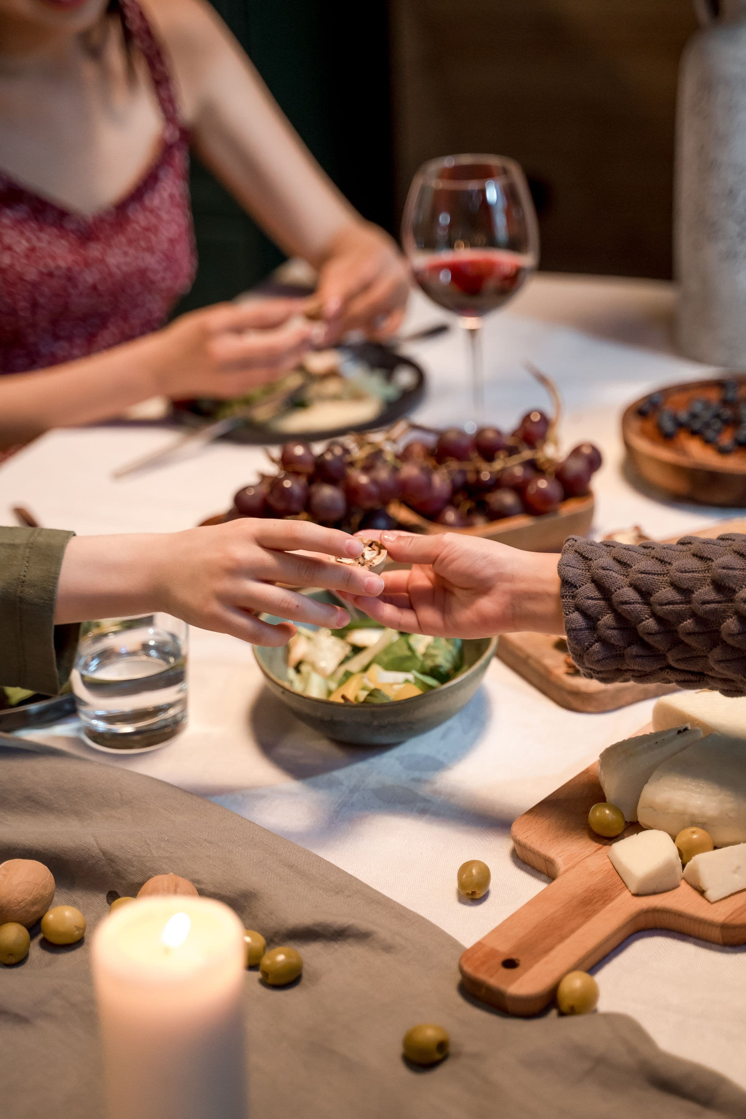 hands passing a dish across a candlelit table, wine and plates around them