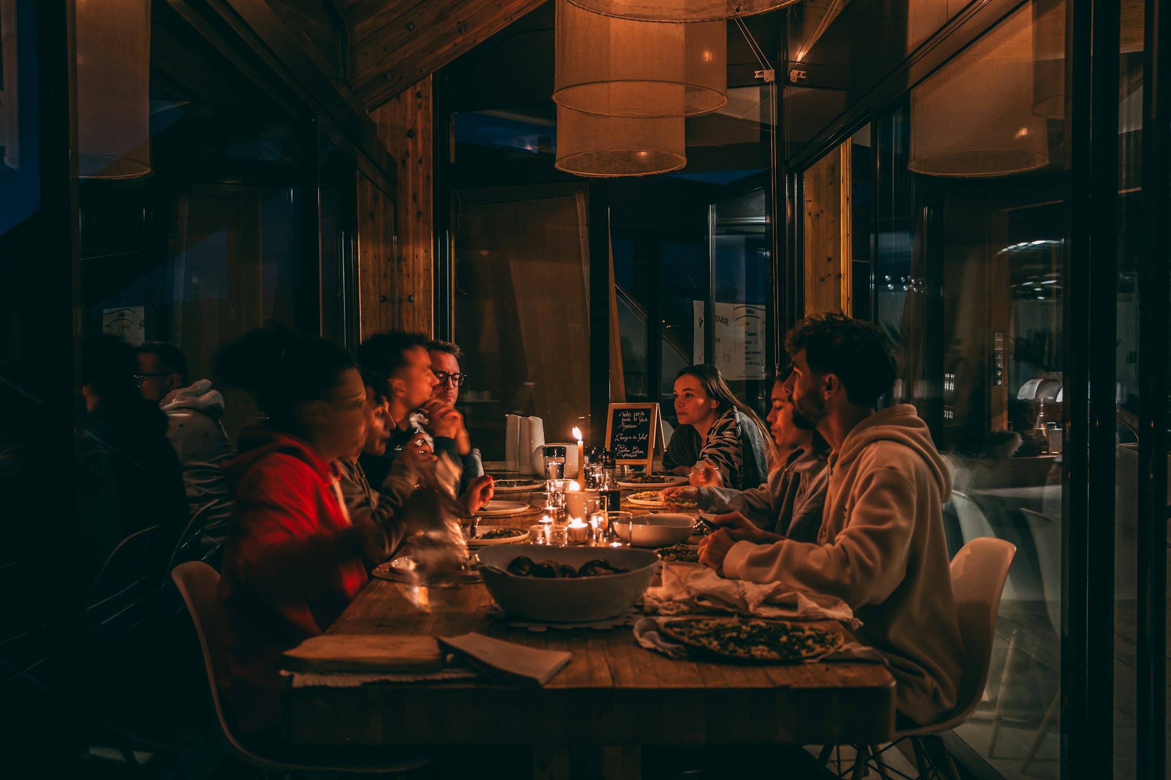 a long table at night under timber and lamplight, candles down the middle