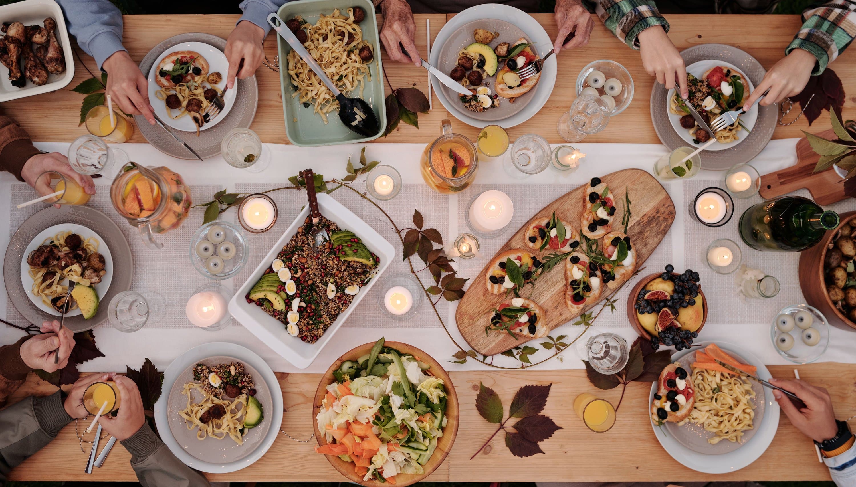 a long table from above, shared platters and candles down the middle, hands reaching in from both sides