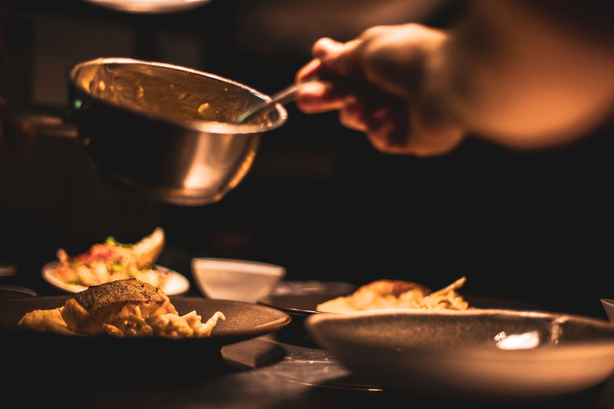 hands plating a dish in a dim kitchen